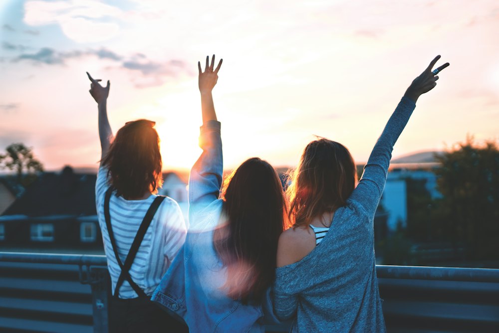 Three friends with arms raised on a rooftop at sunset